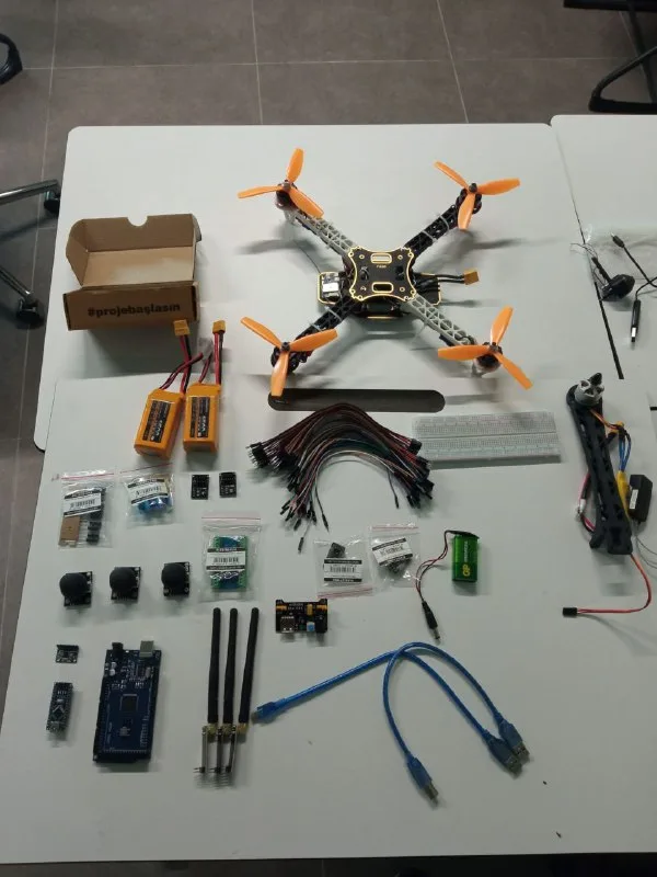 A quadcopter frame, LiPo batteries, cables and electronic boards laid out on a table