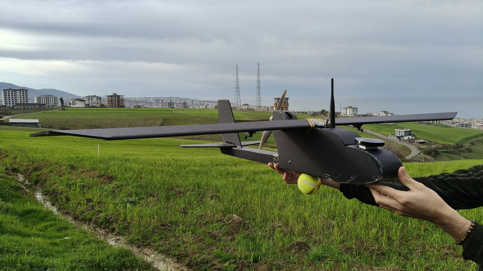 A black model plane about to be hand-launched over a green field